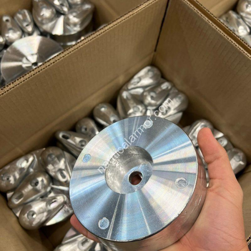 Nautical Armor machined circular propeller anode held in hand with finished anodes in the background.