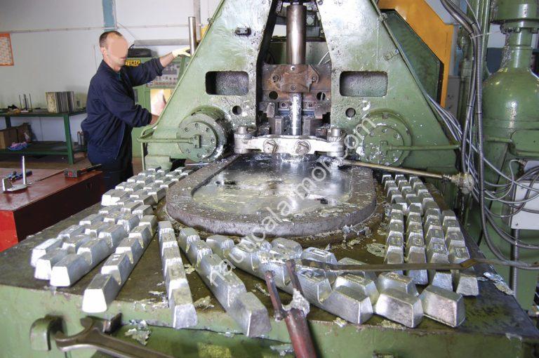 Nautical Armor zinc anode production machine with cast anodes on the table in a foundry setting. Zinc high-pressure injection machine (worker face blurred)