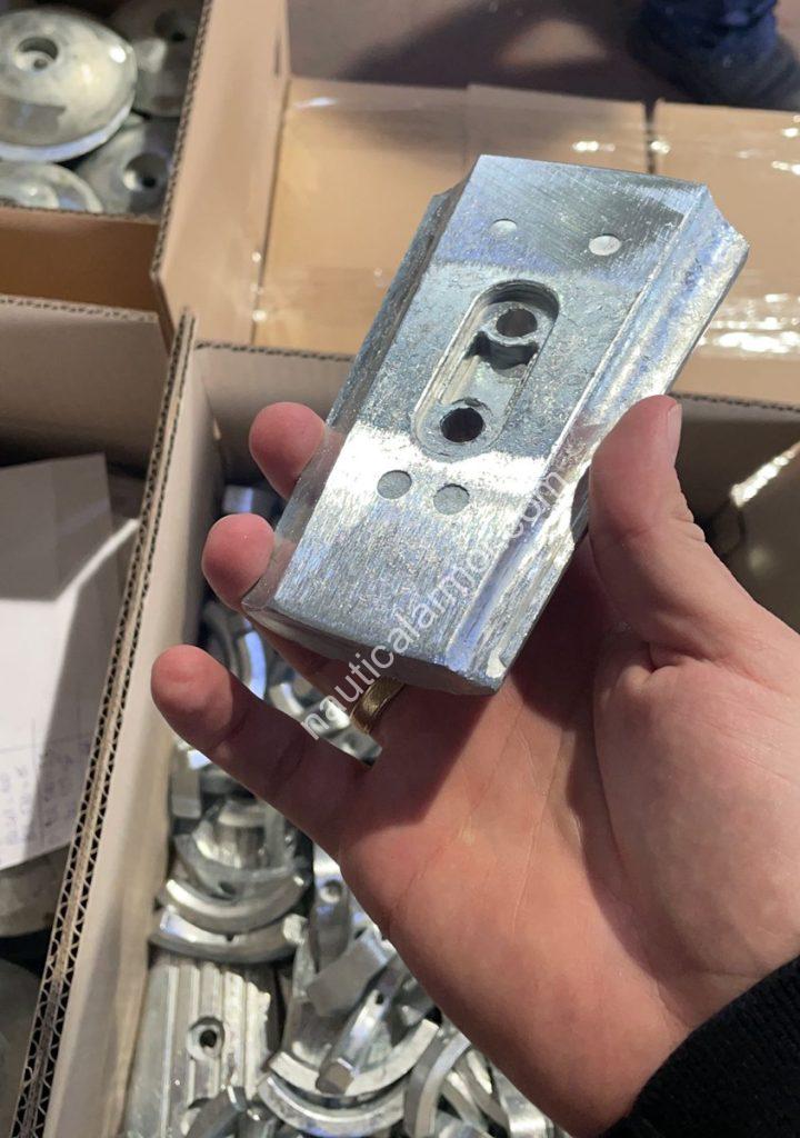 Hand holding a machined sacrificial anode VP compatible 800733 above open boxes filled with anodes in a warehouse.