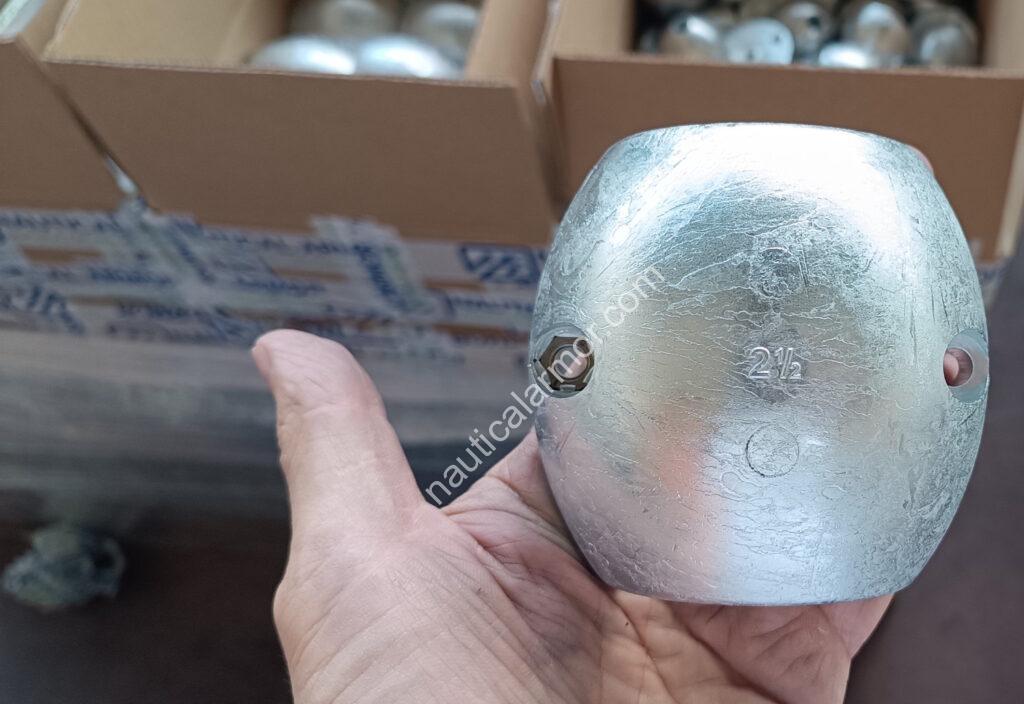 Nautical Armor hand holding a shaft sacrificial anode in front of open packing boxes.