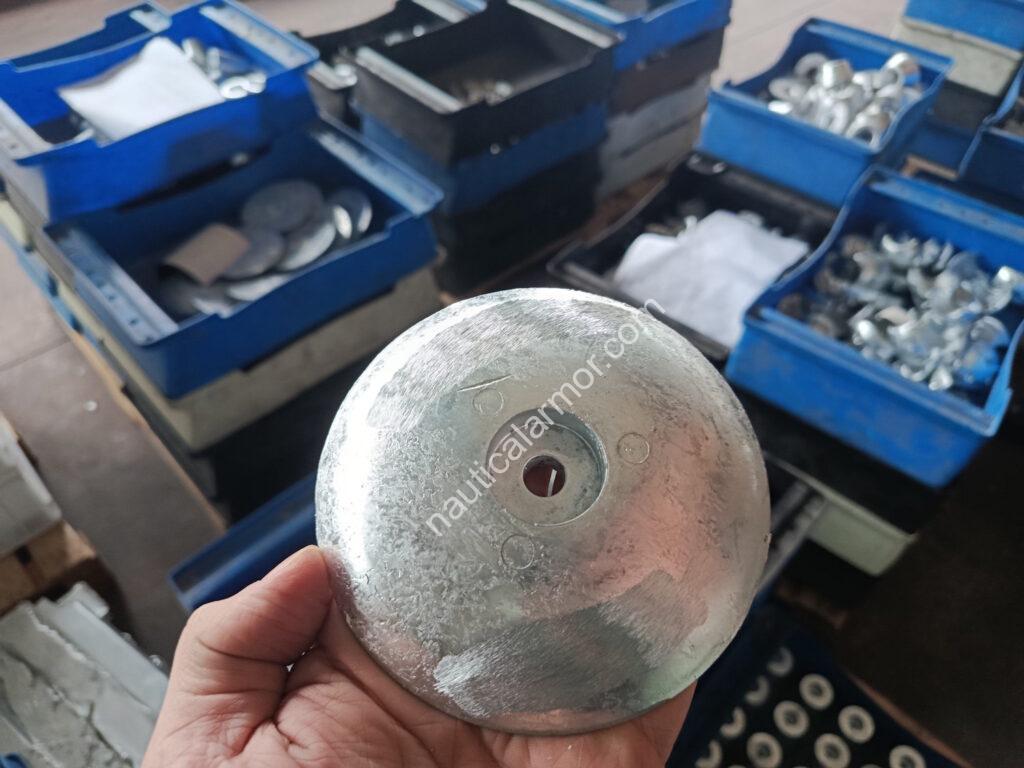 Nautical Armor founder holding zinc rudder anode in a warehouse, with bins of anodes in the background waiting for the inspection.