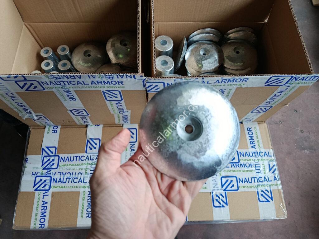 Nautical Armor hand holding a rudder anode above Nautical Armor branded boxes filled with anodes.